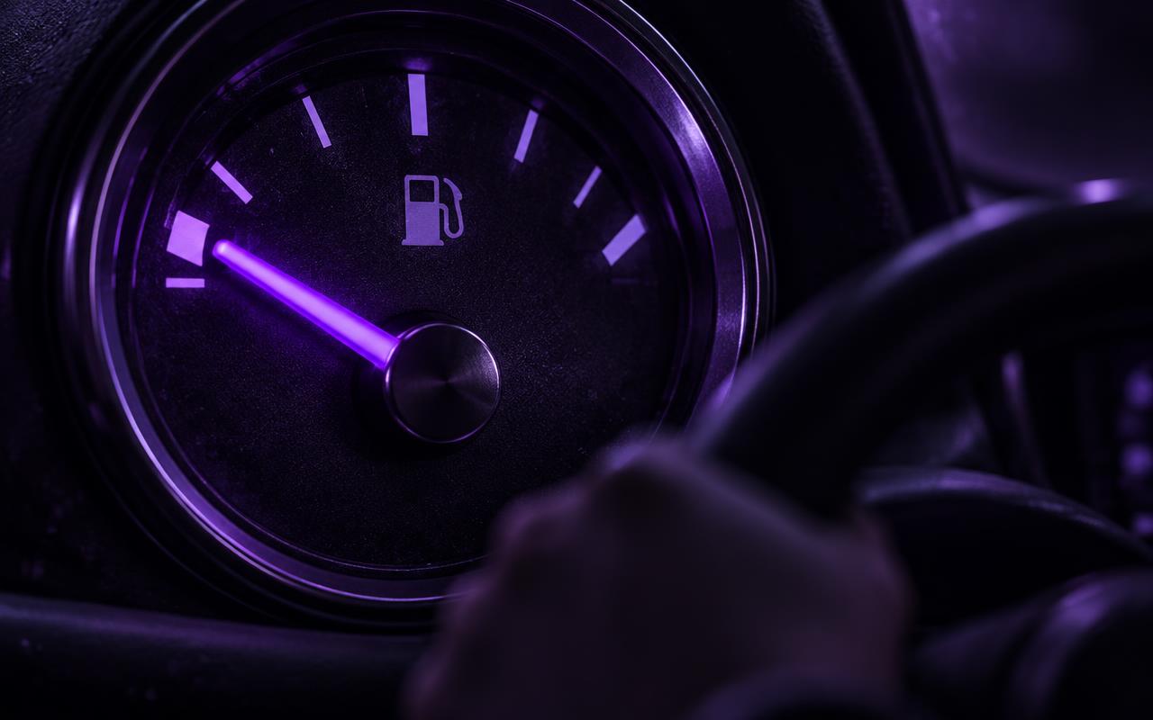Vista de dentro de um táxi à noite, com o ponteiro do marcador de combustível brilhando violeta e apontando para quase vazio, enquanto as mãos do motorista seguem no volante olhando para a estrada escura à frente, representando decidir investimento sem olhar para os próprios dados.